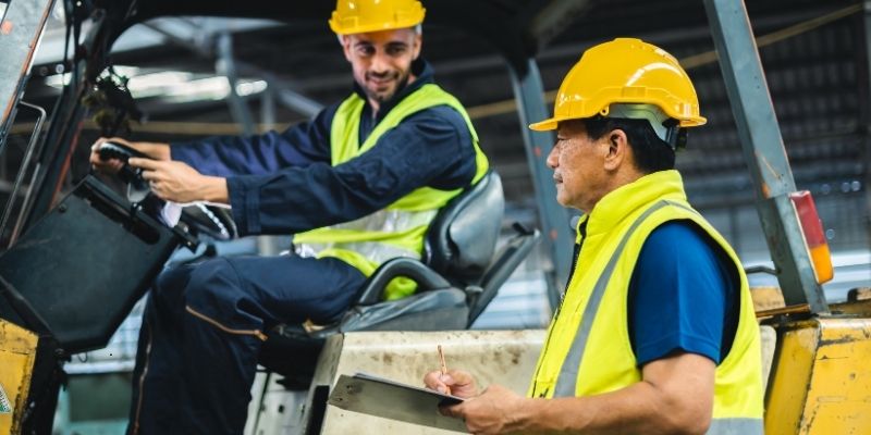 Supervisor inspecting a forklift with an operator, reviewing safety and forklift maintenance procedures in a warehouse.